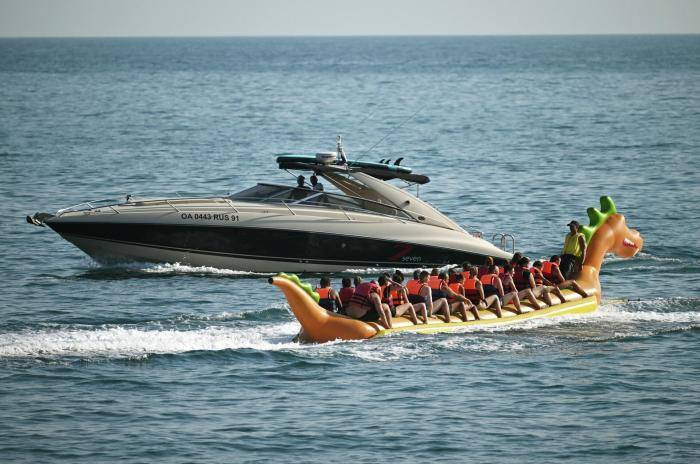 Люди катаются на надувном банане в виде дракона на море